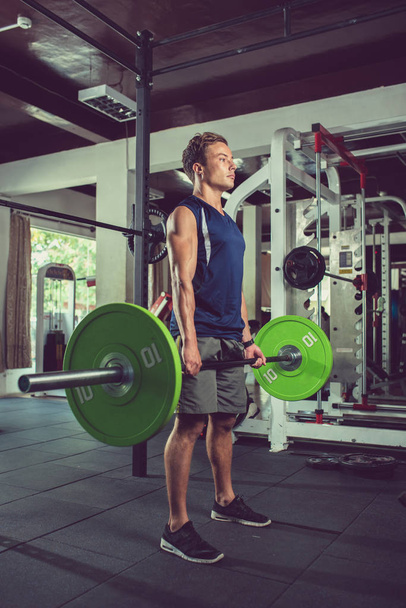 Handsome young man working out with heavy weights in gym - Photo, Image
