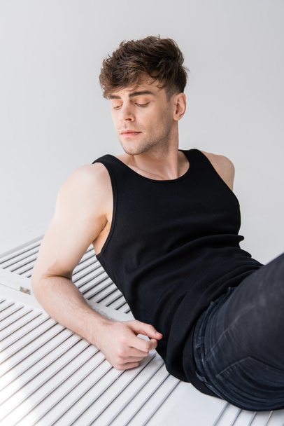 handsome man in black sleeveless shirt lying on grey - Foto, Bild