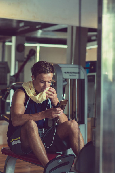 Fit young man wiping face with towel and checking phone between sets - 写真・画像