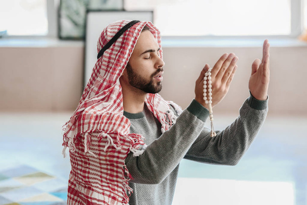 Young Muslim man praying indoors - Фото, изображение