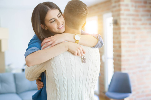 Jeune couple déménageant dans une nouvelle maison, étreignant en amour montrant les clés du nouvel appartement souriant très heureux
 - Photo, image