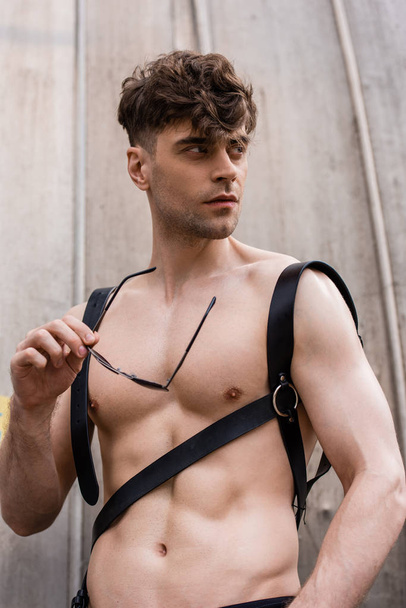 sexy shirtless man in sword belt holding sunglasses and looking away - Фото, зображення