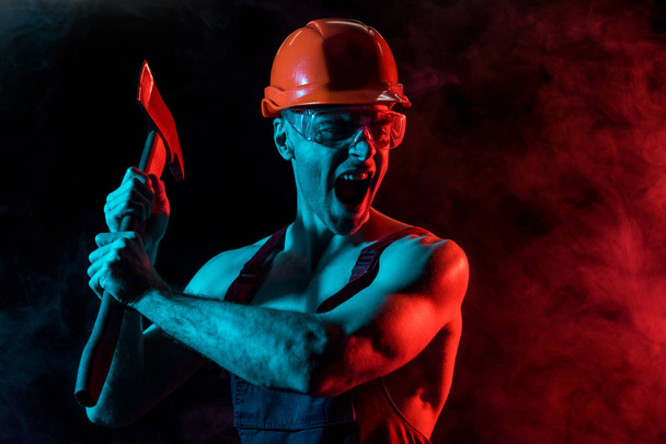 worried shirtless fireman in hardhat and protective goggles holding flat head axe and screaming in smoke on black - Fotó, kép