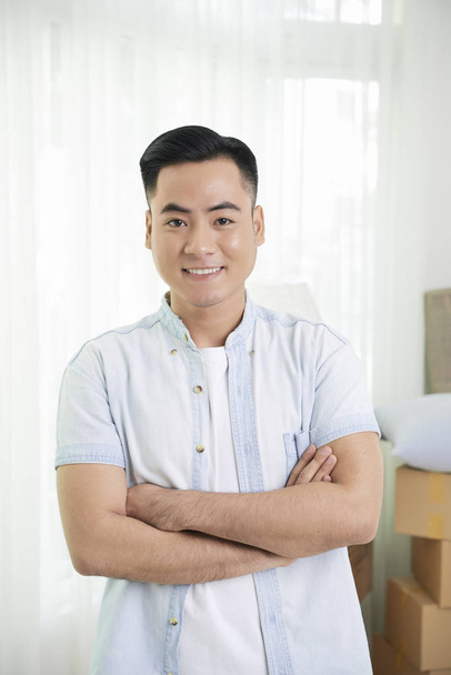 Portrait of happy handsome Vietnamese apartment owner standing in his living room - 写真・画像