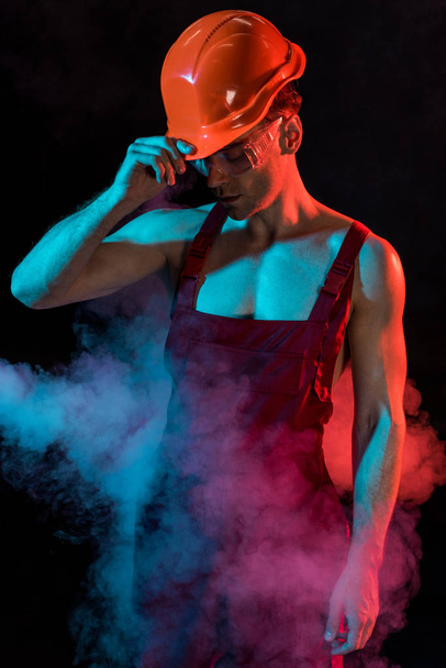 sexy shirtless fireman in overall and hardhat in smoke on black - Foto, immagini