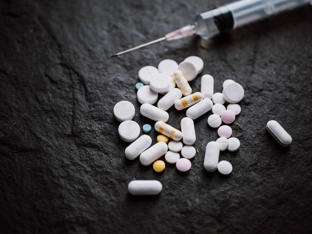 різноманітні барвисті фармацевтичні таблетки таблетки та капсули з гіпотермічним шприцом для введення голки на фоні чорного каменю. аптека і препарат для концепції лікування
 - Фото, зображення