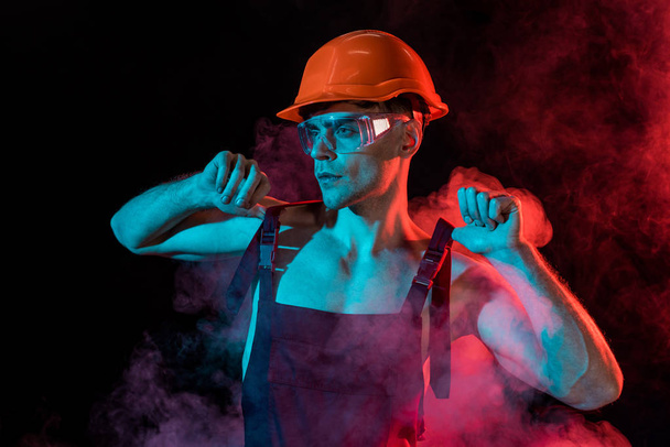 sexy shirtless fireman in overall and hardhat in smoke on black - Foto, afbeelding