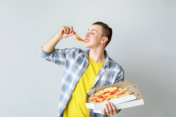 Handsome man eating tasty pizza on light background - Photo, Image