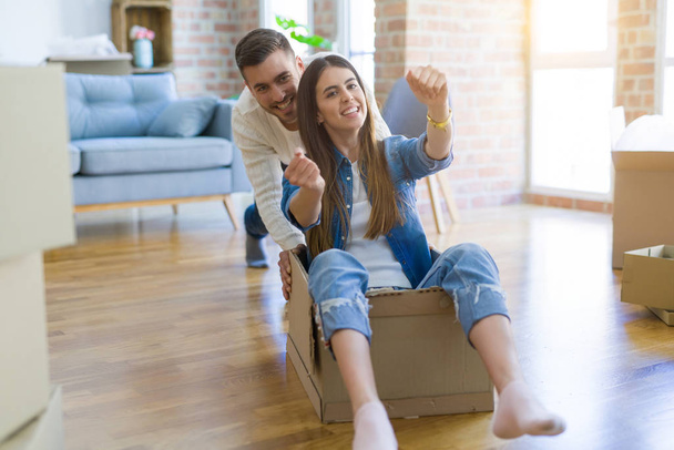 Young couple moving to a new home, having fun riding cardboard boxes - Фото, изображение