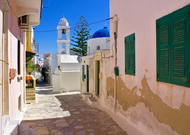 Beautiful peaceful stone paved empty alley, colorful houses and white chapel with blue dome at noon time, Tinos island, Cyclades, Greece. - Photo, Image