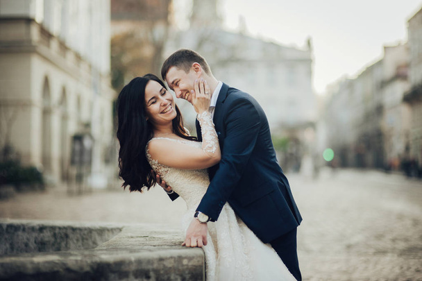 Happy groom and elegant bride in lace wedding dress posing on city street  - Zdjęcie, obraz