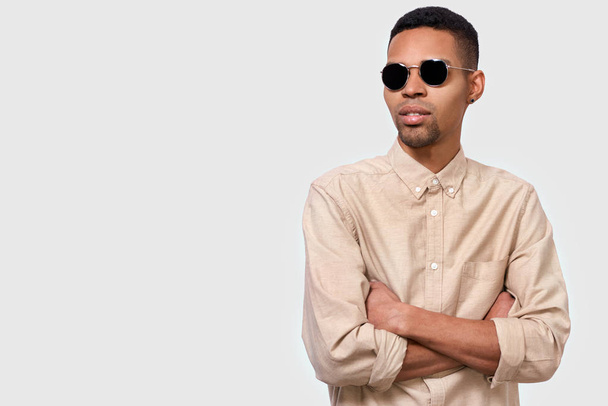 Horizontal studio image of serious young African American man wearing casual shirt keeps crossed hands, looking away over white studio background. Thoughtful male student thinking about exams. People - Φωτογραφία, εικόνα