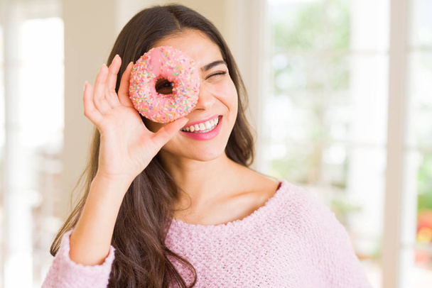 Beautiful young woman smiling looking through pink donut on the eye - 写真・画像