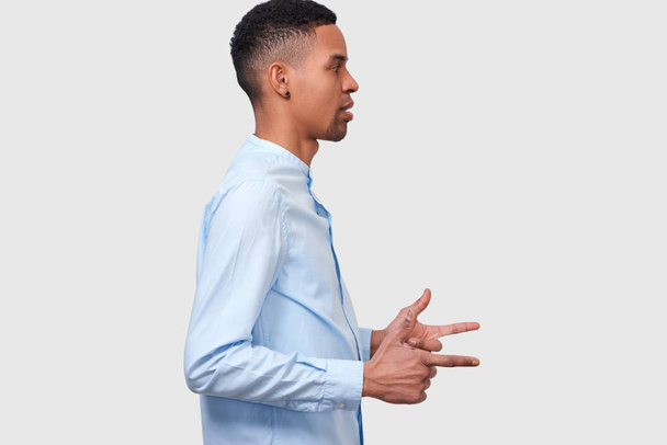 Side view shot of young serious African American male in eyeglasses indicates aside with fore finger, looking at blank copy space, demonstrates something for your promotion. People, emotion concept - Zdjęcie, obraz
