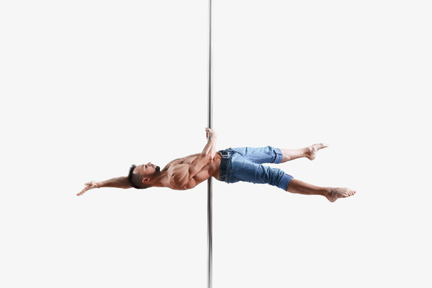 Young pole dance athlete does trick on the white background. Muscular white male sportsman practicing pole dancing.  - Foto, immagini