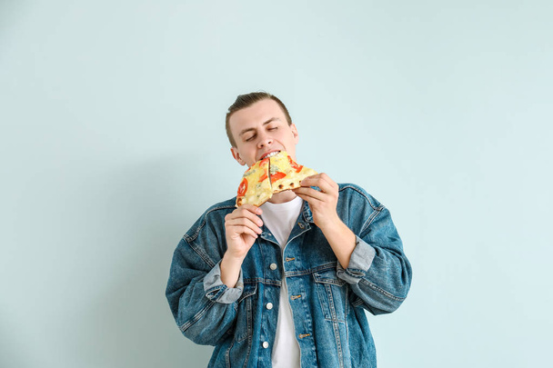 Pohledný člověk, který na světle pozadí konzumní chutnou pizzu - Fotografie, Obrázek