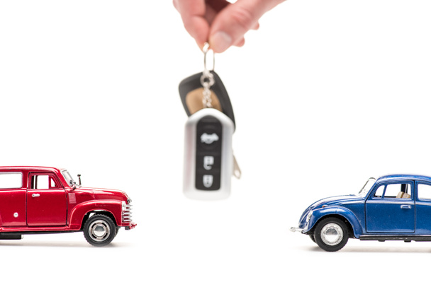 Ausgeschnittene Ansicht eines Mannes mit Schlüssel in der Nähe von Spielzeugautos auf weiß - Foto, Bild