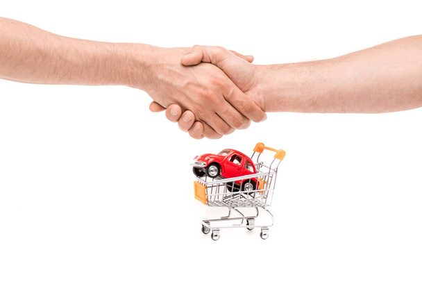 bijgesneden beeld van de man schudden handen in de buurt van speelgoed auto in winkelwagen geïsoleerd op wit - Foto, afbeelding