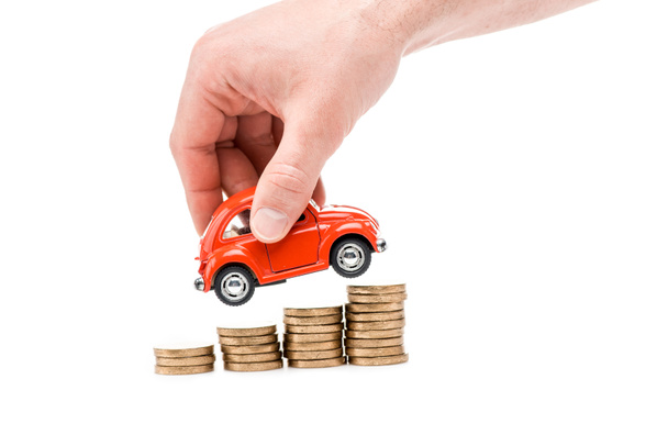 cropped view of man holding red toy car above coins isolated on white - Fotó, kép