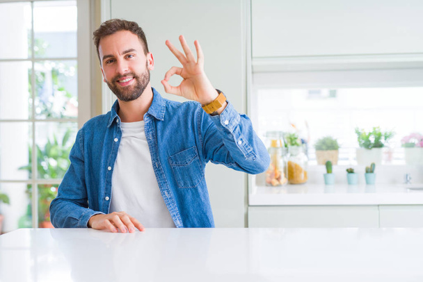 Handsome man at home smiling positive doing ok sign with hand and fingers. Successful expression. - Фото, изображение