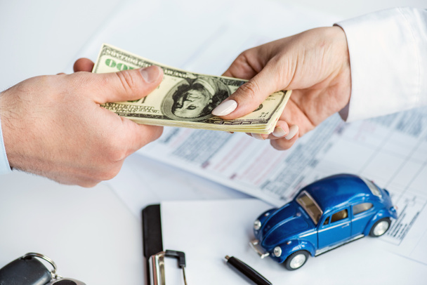 обрезанный вид мужчины и женщины с долларовыми банкнотами возле игрушечного автомобиля, буфера обмена и документов
 - Фото, изображение
