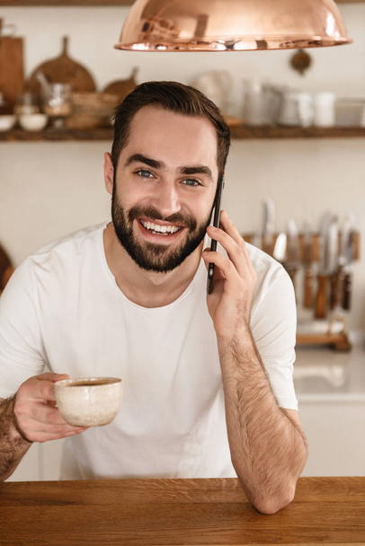 Portrait of happy brunette man 20s drinking coffee and using sma - Photo, Image
