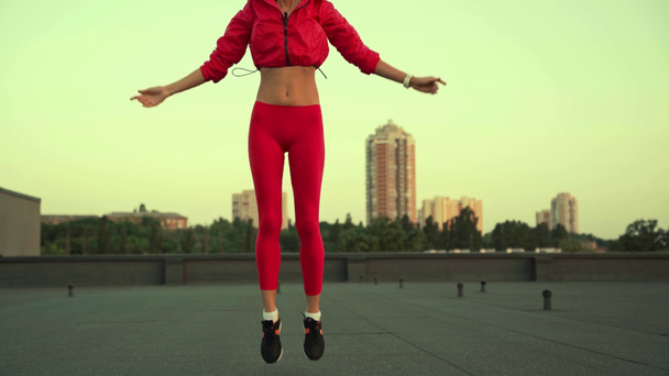 beautiful sportswoman looking at camera, running on rooftop and jumping, holding hands over head - Кадри, відео
