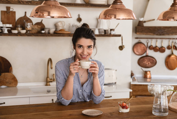 Photo of smiling brunette woman 20s drinking coffee while having - Photo, image