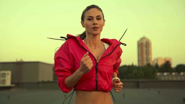 charmante Sportvrouw in sportkleding die op het dak draait met een glimlach, kijkend naar de camera - Video
