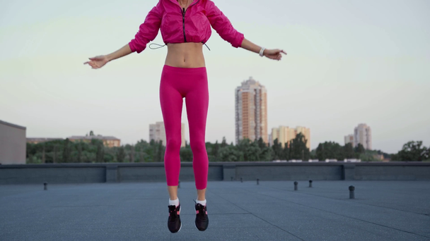 low angle view of beautiful sportswoman in sportswear holding hands over head, jumping  on rooftop - Кадри, відео