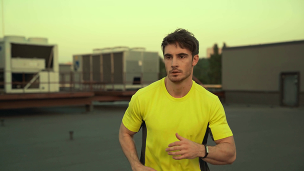 przystojny sportowiec w żółtym odzieży sportowej biegną na dachu - Materiał filmowy, wideo