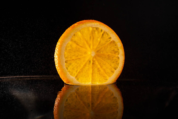 juicy orange slice falls into water with splashes on a black background with reflection - 写真・画像