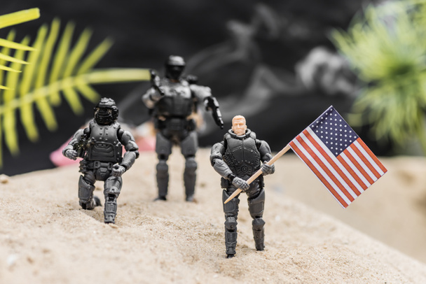 selektywne skupienie zabawnych żołnierzy z bronią posiadając amerykańską flagę na wydmach piaskowych - Zdjęcie, obraz