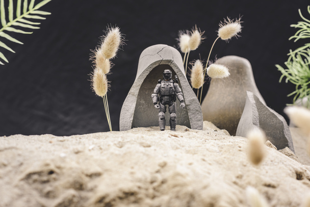 selective focus of toy soldier with gun standing near caves on sand dune on black background - 写真・画像