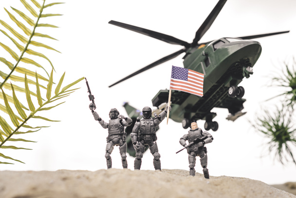 空のヘリコプターの近くに銃とアメリカの旗を持つ砂丘のプラスチックおもちゃの兵士 - 写真・画像