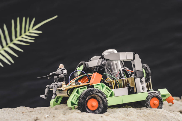 soldat jouet avec pistolet assis sur la voiture sur une dune de sable sur fond noir
 - Photo, image