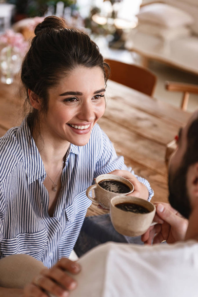 Image of happy brunette couple drinking coffee together while si - 写真・画像