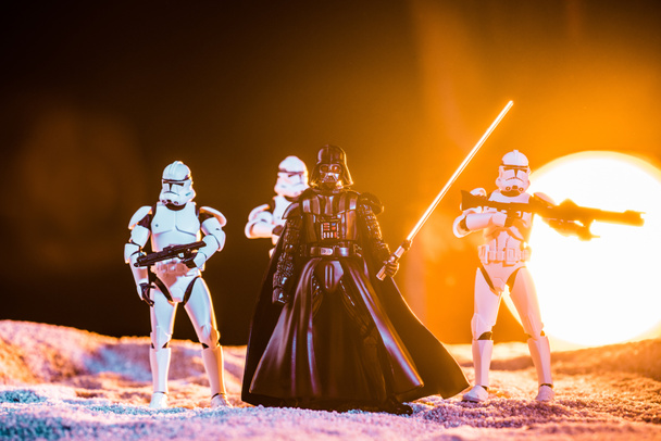 white imperial stormtroopers with guns and  Darth Vader with lightsaber on black background with bright sun - Фото, изображение
