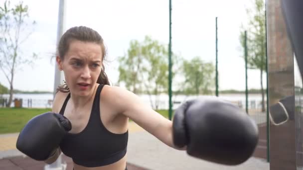 Lassított. Fiatal nő bokszoló képzés lyukasztó zsák utcai város edzőpálya. Egyenletes szemcsésedik, szembenéz zár megjelöl. Önvédelmi csapat. - Felvétel, videó