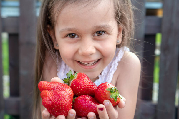 Λευκό κορίτσι με μακριά μαύρα μαλλιά που κρατά φράουλες. - Φωτογραφία, εικόνα