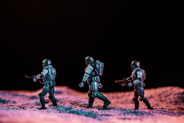 στρατιώτες παιχνίδι που περπατούν με όπλο στον πλανήτη στο διάστημα απομονώνονται σε μαύρο - Φωτογραφία, εικόνα