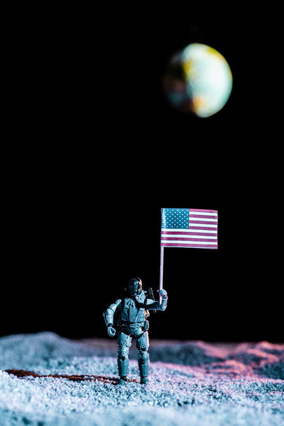 игрушечный солдат держит национальный американский флаг в космосе с планетой Земля на черном фоне
 - Фото, изображение