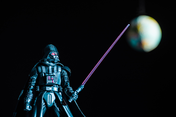 selective focus of Darth Vader figurine with lightsaber on black background with planet Earth - Фото, изображение