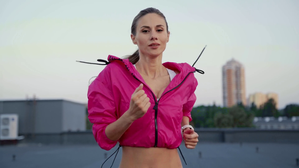 mooie Sportvrouw in sportkleding die op het dak draait met een glimlach, kijkend naar de camera - Video