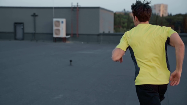 Widok z tyłu sportowca w odzieży sportowej biegną na dachu i schodów - Materiał filmowy, wideo