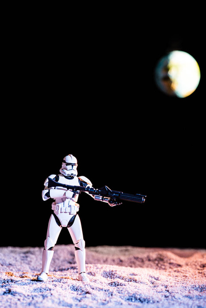 white imperial stormtrooper with gun on black background with blurred planet Earth - Φωτογραφία, εικόνα