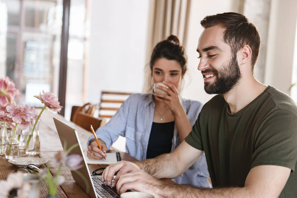 Image of adorable brunette couple working on laptop together whi - Фото, зображення