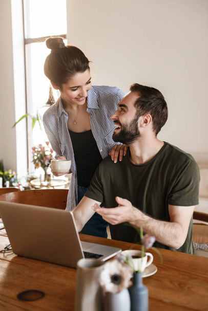 Image of smiling brunette couple working on laptop together whil - Φωτογραφία, εικόνα
