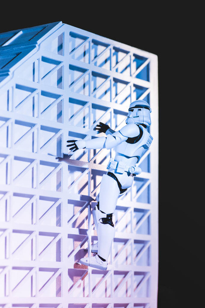 white plastic Imperial Stormtrooper climbing white textured wall isolated on black - Foto, Bild