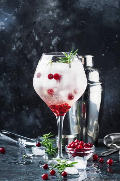 Cranberry cocktail with ice, fresh rosemary and red berries in big wine glass, bar tools, gray bar counter background, copy space, selective focus - Fotó, kép